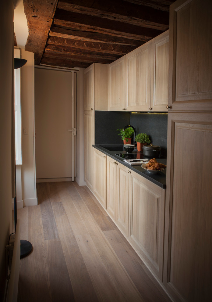 Design ideas for a small traditional single-wall open plan kitchen in Paris with an integrated sink, beaded cabinets, light wood cabinets, black splashback, limestone splashback, integrated appliances, light hardwood flooring, no island, brown floors, black worktops and marble worktops.