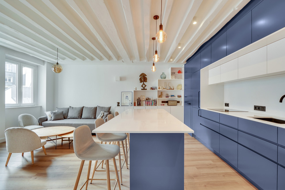 Modern inredning av ett vit linjärt vitt kök med öppen planlösning, med en undermonterad diskho, släta luckor, blå skåp, vitt stänkskydd, integrerade vitvaror, ljust trägolv, en köksö och beiget golv