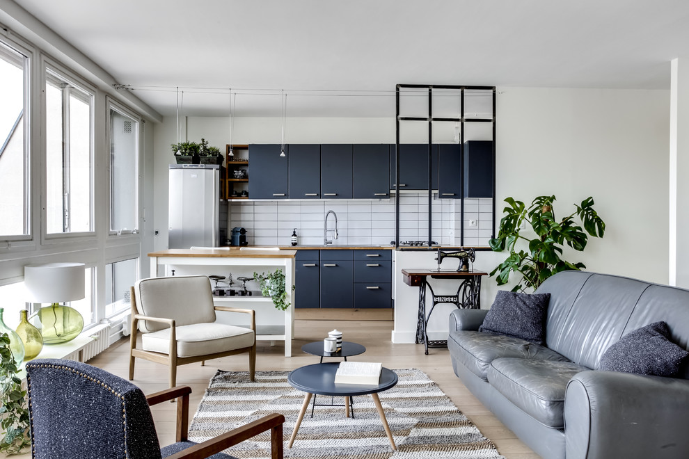 Scandi single-wall open plan kitchen in Paris with flat-panel cabinets, blue cabinets, wood worktops, white splashback, metro tiled splashback, stainless steel appliances, light hardwood flooring, an island and beige floors.