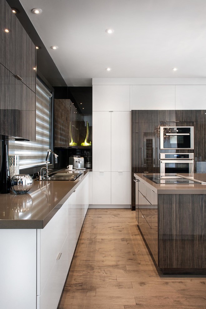 Offene, Mittelgroße Moderne Küche in L-Form mit flächenbündigen Schrankfronten, weißen Schränken, Küchengeräten aus Edelstahl, braunem Holzboden, Kücheninsel, Doppelwaschbecken, Quarzit-Arbeitsplatte und Küchenrückwand in Schwarz in Montreal
