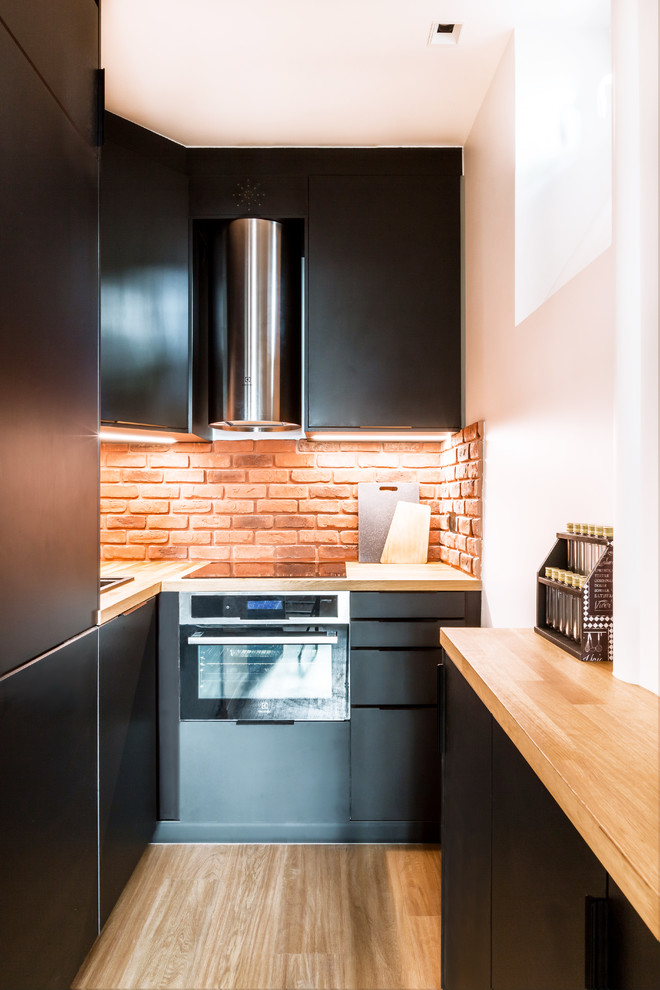Foto på ett mellanstort funkis brun kök, med en undermonterad diskho, luckor med profilerade fronter, svarta skåp, träbänkskiva, orange stänkskydd, stänkskydd i tegel, rostfria vitvaror, mellanmörkt trägolv, en köksö och brunt golv