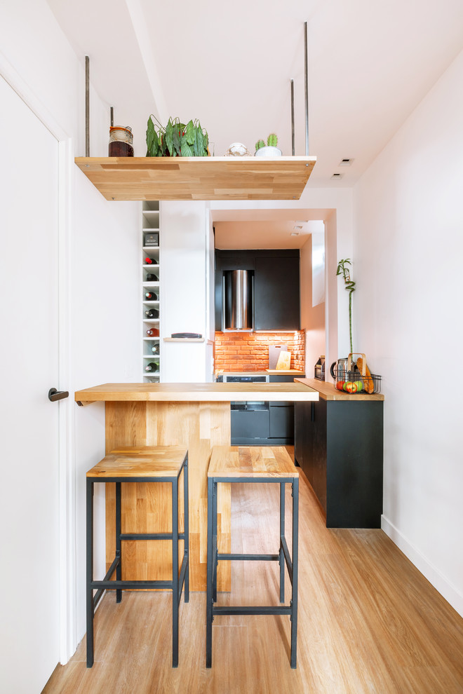 パリにあるお手頃価格の中くらいなトロピカルスタイルのおしゃれなキッチン (アンダーカウンターシンク、インセット扉のキャビネット、黒いキャビネット、木材カウンター、赤いキッチンパネル、レンガのキッチンパネル、無垢フローリング、茶色い床、茶色いキッチンカウンター、シルバーの調理設備) の写真