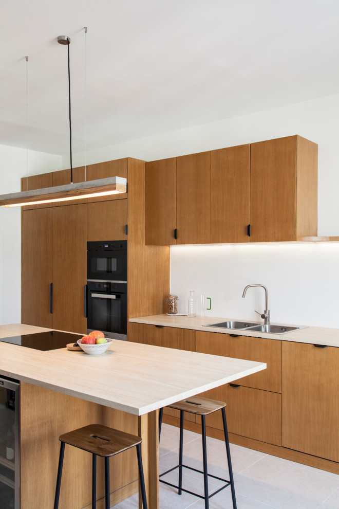 Zweizeilige Moderne Küche mit Doppelwaschbecken, flächenbündigen Schrankfronten, hellbraunen Holzschränken, schwarzen Elektrogeräten, Kücheninsel, weißem Boden und beiger Arbeitsplatte in Paris