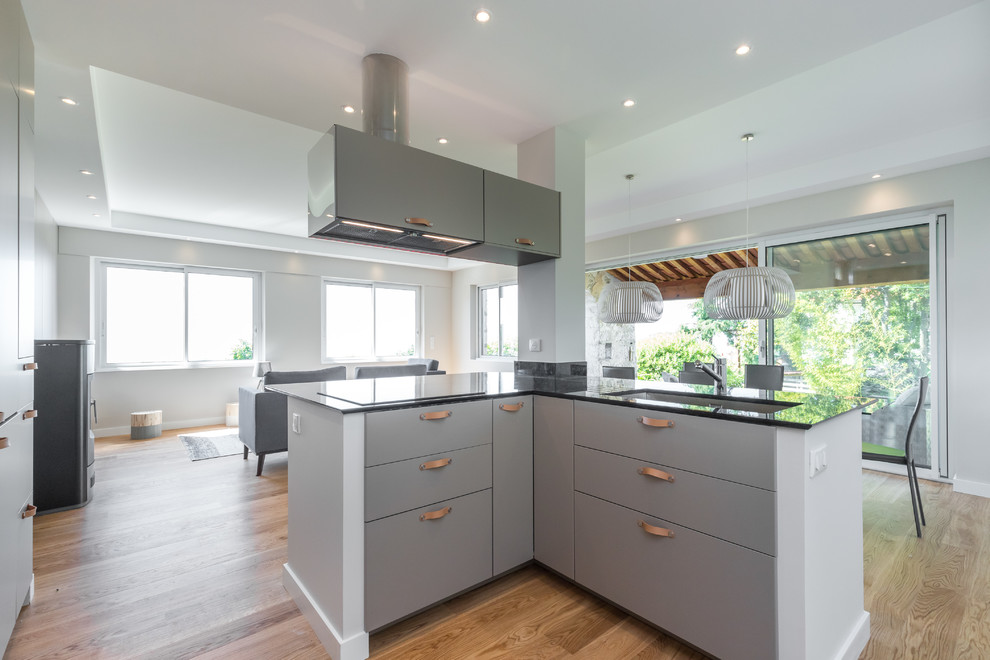 Design ideas for a large contemporary u-shaped open plan kitchen in Nice with flat-panel cabinets, beige cabinets, granite worktops, multiple islands, black worktops, an integrated sink, black appliances, beige floors and light hardwood flooring.