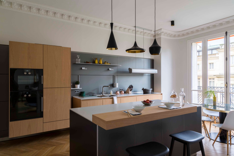 Foto di una cucina minimal con lavello sottopiano, ante lisce, ante in legno chiaro, elettrodomestici neri, pavimento in legno massello medio, pavimento marrone e top grigio
