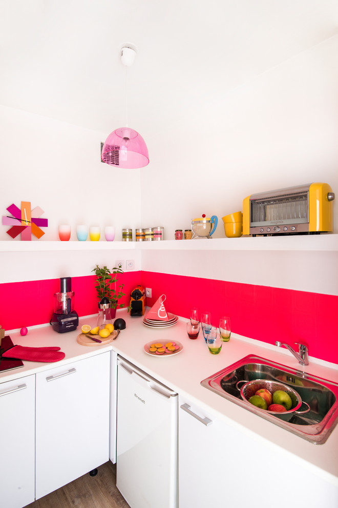 Foto på ett litet, avskilt funkis l-kök, med en nedsänkt diskho, släta luckor, vita skåp, rosa stänkskydd, vita vitvaror och mörkt trägolv