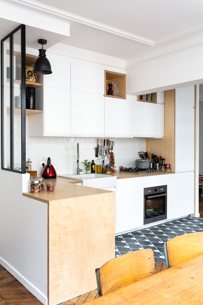 This is an example of a small scandinavian l-shaped kitchen/diner in Paris with a belfast sink, flat-panel cabinets, white cabinets, wood worktops, white splashback, ceramic splashback, stainless steel appliances, cement flooring, no island, grey floors and beige worktops.