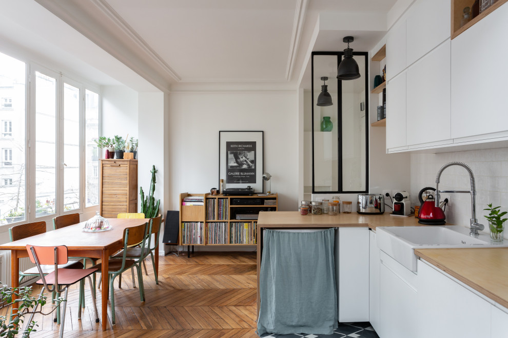 パリにある北欧スタイルのおしゃれなキッチン (エプロンフロントシンク、フラットパネル扉のキャビネット、白いキャビネット、木材カウンター、白いキッチンパネル、無垢フローリング、ベージュのキッチンカウンター) の写真