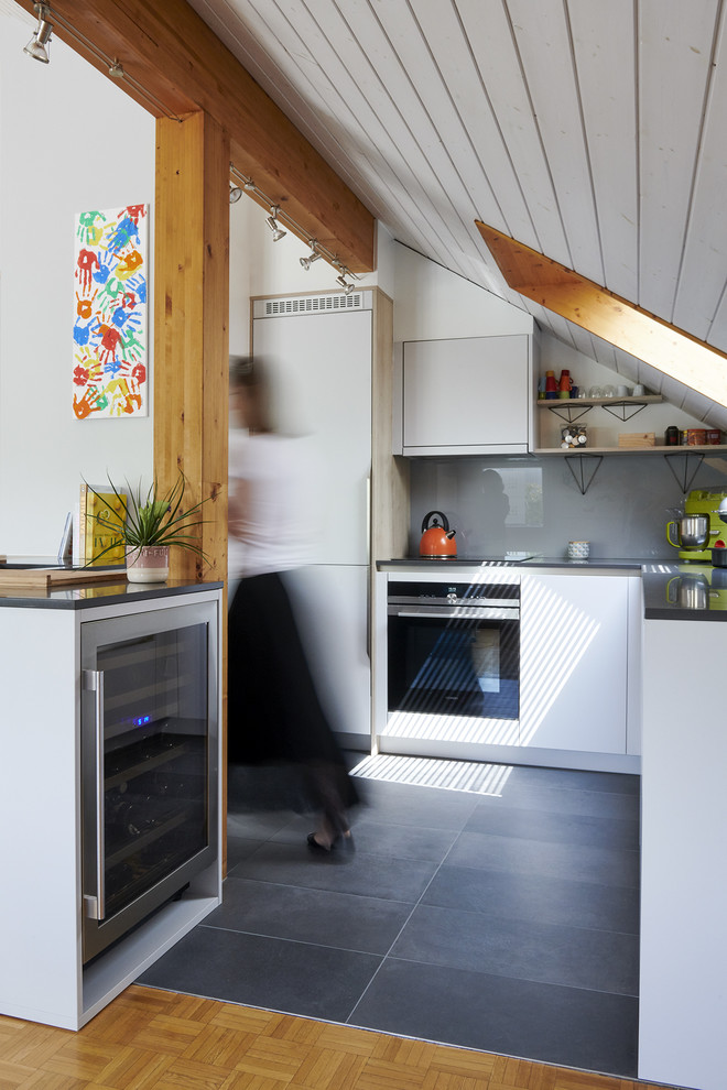 Aménagement d'une petite cuisine ouverte scandinave en L avec un placard à porte plane, des portes de placard blanches, une crédence grise, une crédence en feuille de verre, un électroménager noir, îlot, un sol gris et un plan de travail gris.