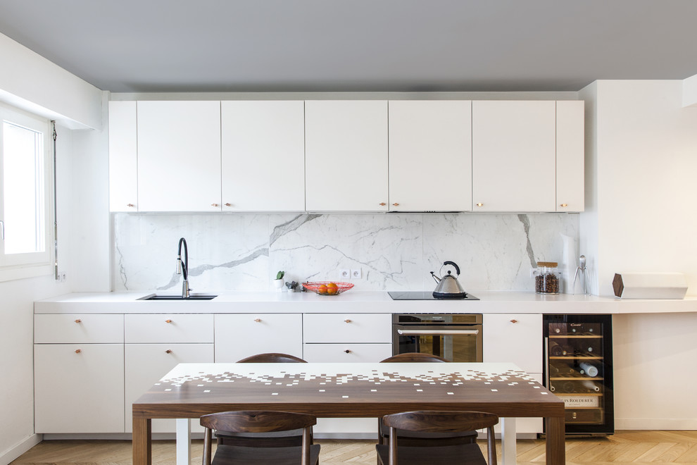 Idéer för ett modernt vit linjärt kök och matrum, med en undermonterad diskho, släta luckor, vita skåp, vitt stänkskydd, stänkskydd i sten och ljust trägolv