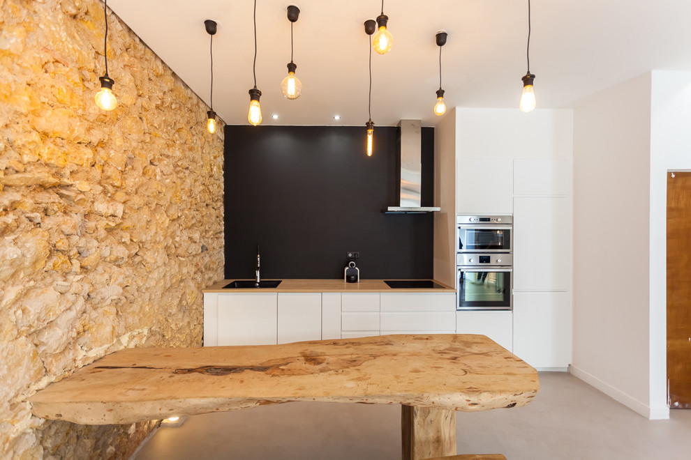Inspiration for a rustic single-wall concrete floor and gray floor open concept kitchen remodel in Marseille with flat-panel cabinets, white cabinets, wood countertops, black backsplash, stainless steel appliances and no island