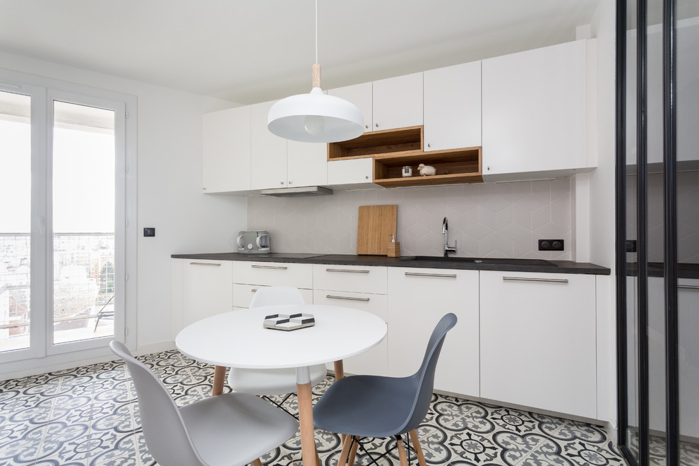 Inspiration for a medium sized contemporary single-wall enclosed kitchen in Paris with a built-in sink, flat-panel cabinets, white cabinets, laminate countertops, white splashback, ceramic splashback, stainless steel appliances, cement flooring, no island, grey floors and black worktops.