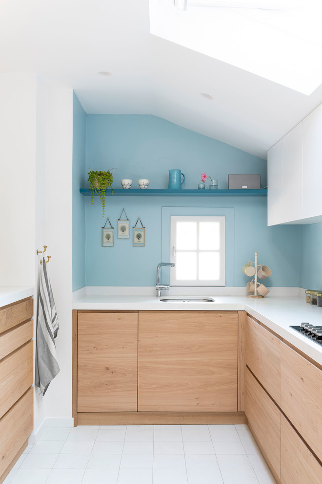 Источник вдохновения для домашнего уюта: угловая кухня в морском стиле с врезной мойкой, плоскими фасадами, светлыми деревянными фасадами, синим фартуком, белым полом, белой столешницей, окном и мойкой у окна