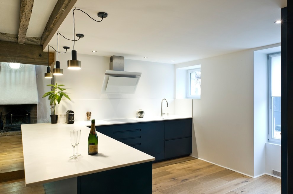 Large contemporary l-shaped kitchen/diner in Paris with an integrated sink, flat-panel cabinets, blue cabinets, composite countertops, white splashback, stainless steel appliances, light hardwood flooring, a breakfast bar, brown floors and white worktops.