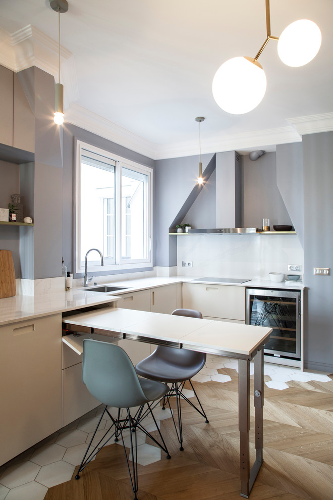 Moderne Wohnküche in L-Form mit Unterbauwaschbecken, flächenbündigen Schrankfronten, beigen Schränken, Küchengeräten aus Edelstahl, braunem Holzboden, Halbinsel, braunem Boden und weißer Arbeitsplatte in Paris