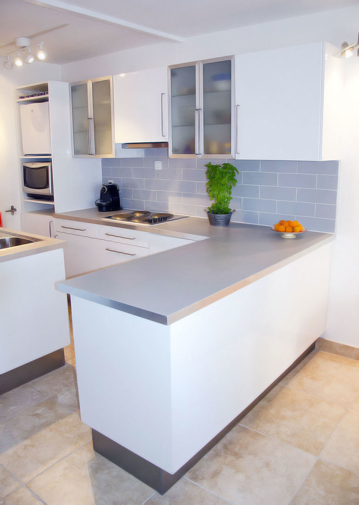 Immagine di una piccola cucina minimalista con lavello sottopiano, ante di vetro, ante bianche, top in laminato, paraspruzzi blu, pavimento con piastrelle in ceramica e penisola