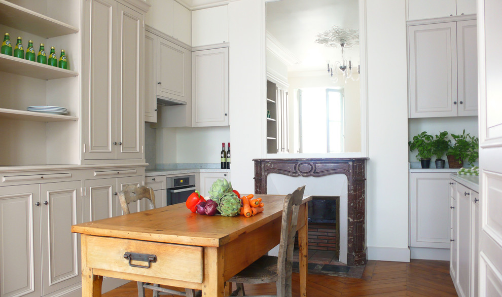 Modelo de cocina bohemia de tamaño medio con puertas de armario beige, salpicadero verde, electrodomésticos con paneles y suelo de madera en tonos medios