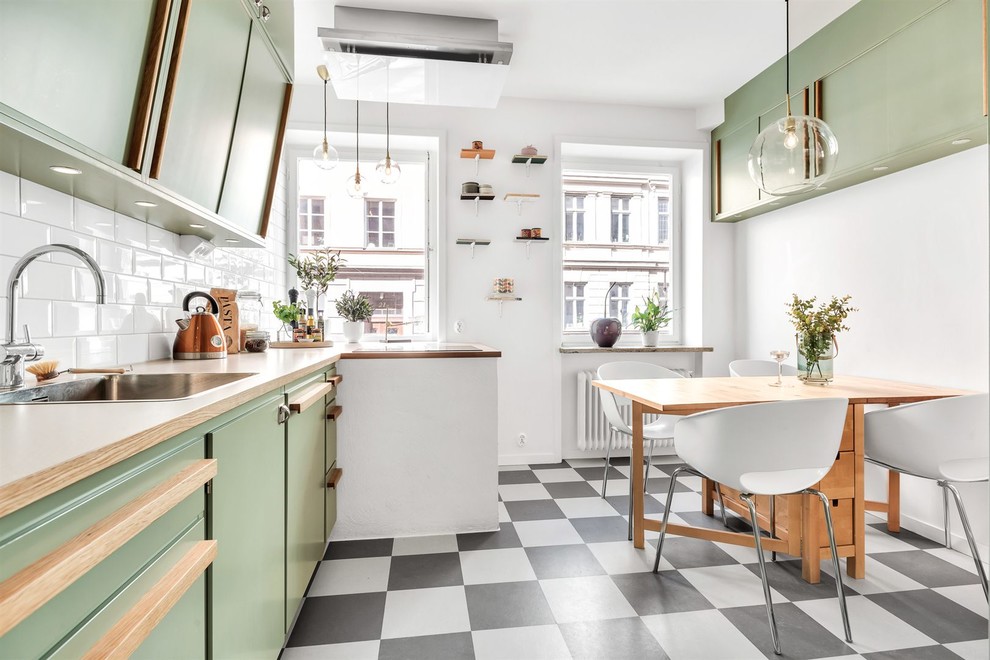 This is an example of a midcentury single-wall kitchen/diner in Stockholm with a built-in sink, flat-panel cabinets, green cabinets, wood worktops, white splashback, metro tiled splashback, integrated appliances, no island, multi-coloured floors and beige worktops.