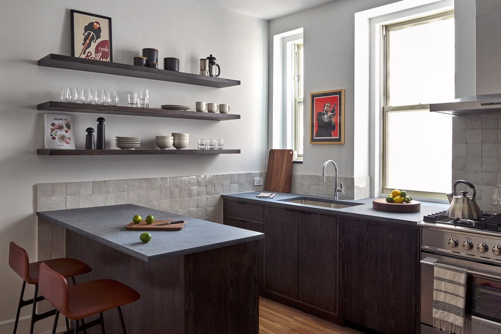 Moderne Küche mit Unterbauwaschbecken, flächenbündigen Schrankfronten, dunklen Holzschränken, Küchenrückwand in Grau, Küchengeräten aus Edelstahl, hellem Holzboden, Halbinsel und grauer Arbeitsplatte in New York