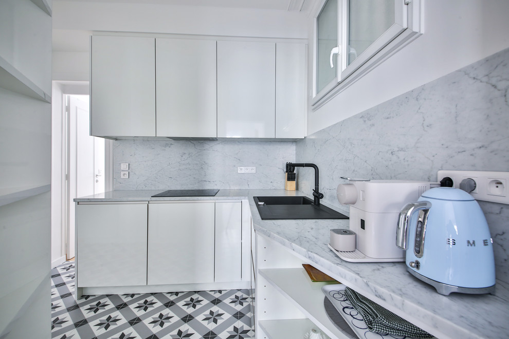 Foto på ett avskilt, litet funkis grå l-kök, med en enkel diskho, släta luckor, vita skåp, granitbänkskiva, grått stänkskydd, stänkskydd i marmor, svarta vitvaror, klinkergolv i keramik och grått golv