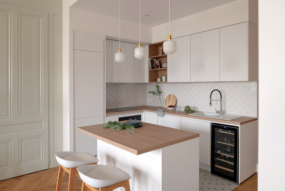 Inredning av ett minimalistiskt litet beige beige l-kök, med en nedsänkt diskho, släta luckor, vita skåp, träbänkskiva, vitt stänkskydd, integrerade vitvaror, en köksö och vitt golv