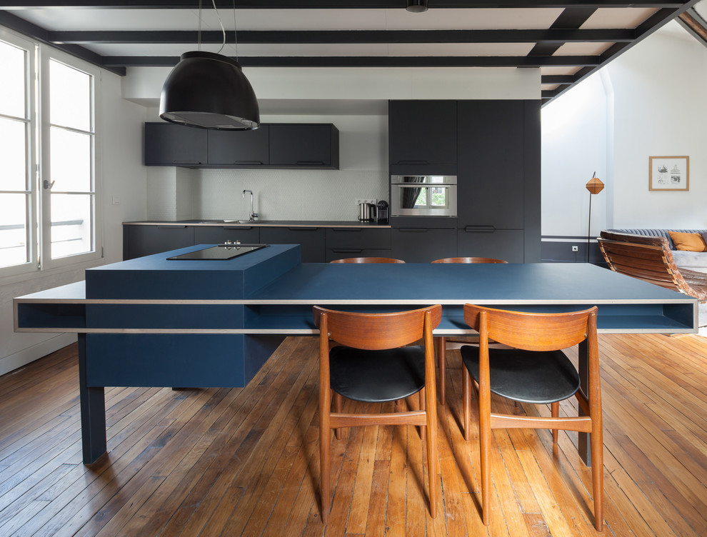 Bild på ett nordiskt blå linjärt blått kök med öppen planlösning, med släta luckor, svarta skåp, rostfria vitvaror, mellanmörkt trägolv, en köksö, en undermonterad diskho, vitt stänkskydd och brunt golv