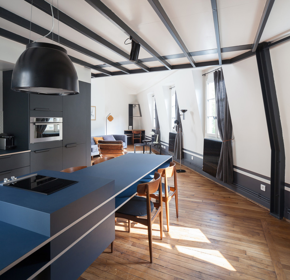 Idée de décoration pour une cuisine ouverte linéaire nordique avec un évier encastré, un placard à porte plane, des portes de placard noires, une crédence blanche, un électroménager en acier inoxydable, un sol en bois brun, îlot, un sol marron et un plan de travail bleu.