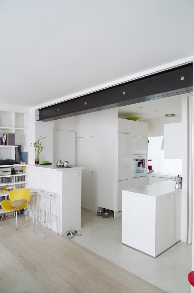 Идея дизайна: угловая кухня-гостиная среднего размера в современном стиле с белыми фасадами, светлым паркетным полом, полуостровом и акцентной стеной