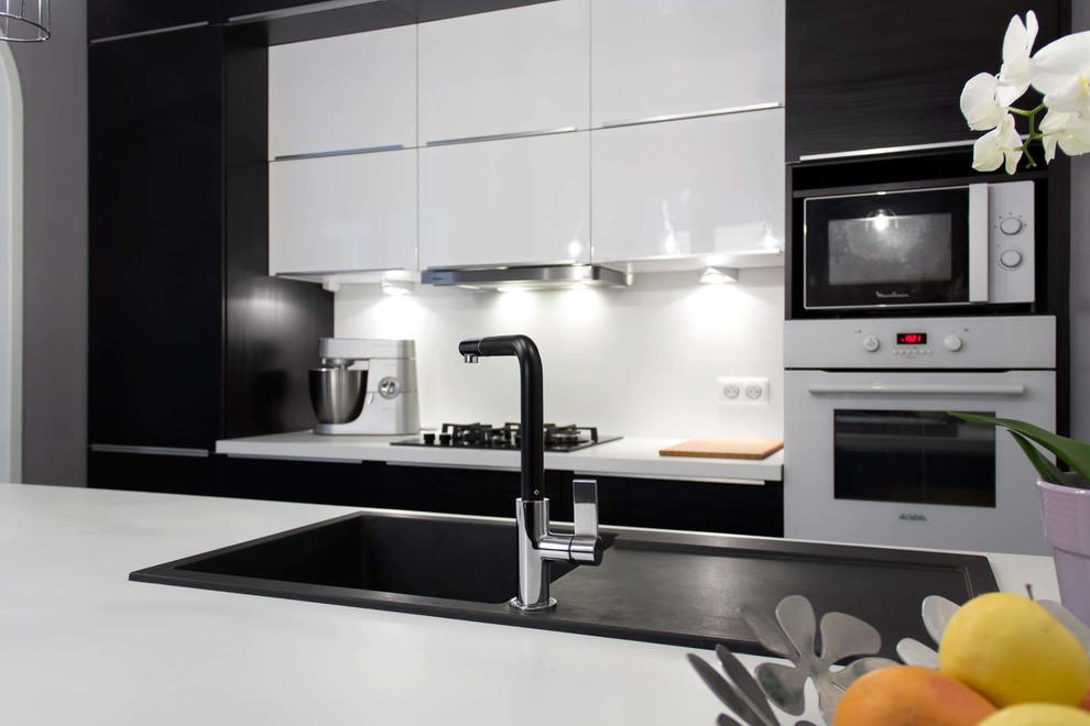 Foto på ett mellanstort funkis kök, med en enkel diskho, släta luckor, vita skåp, laminatbänkskiva, vitt stänkskydd, vita vitvaror, klinkergolv i keramik och en köksö
