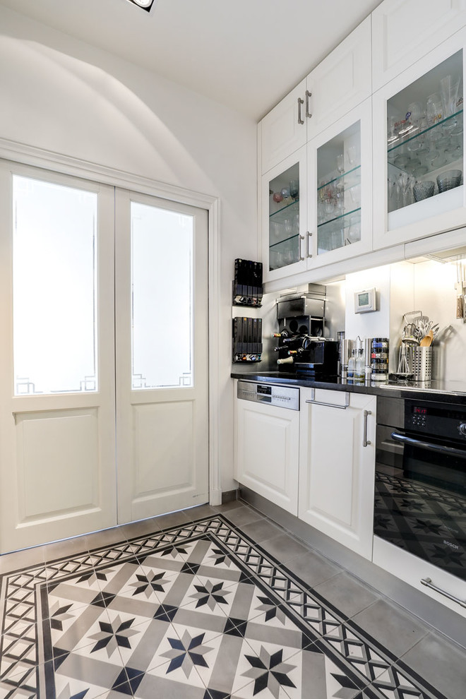 This is an example of a small classic galley open plan kitchen in Paris with a submerged sink, recessed-panel cabinets, white cabinets, granite worktops, white splashback, stainless steel appliances, cement flooring, no island and black worktops.