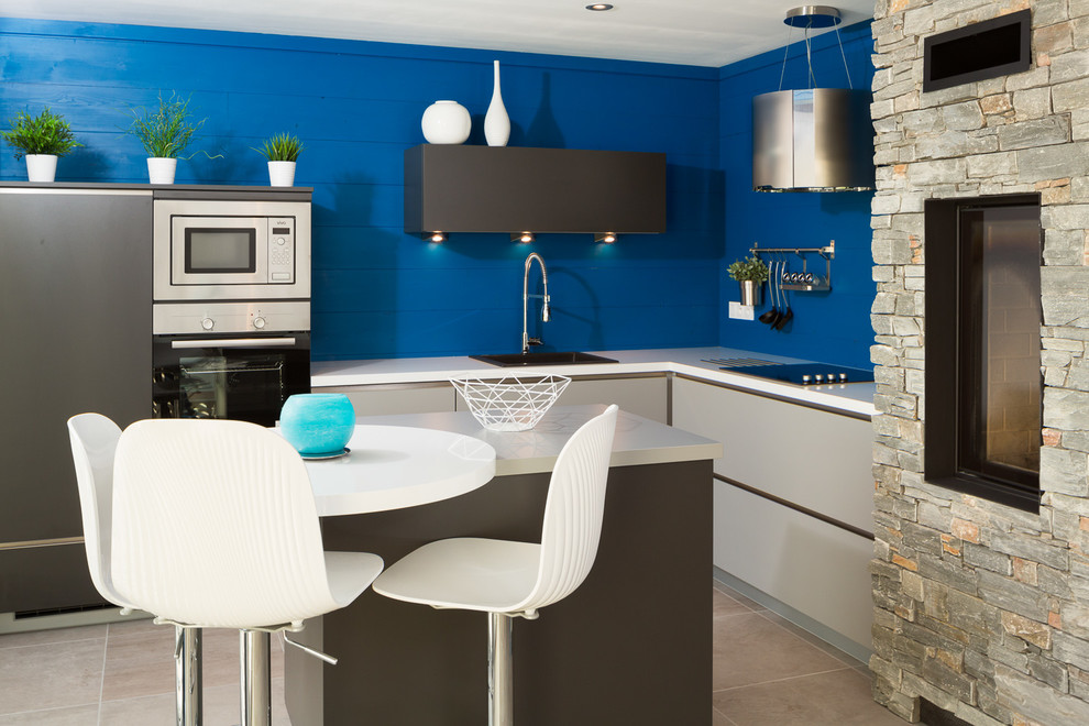 На фото: маленькая угловая кухня в современном стиле с обеденным столом, монолитной мойкой, белыми фасадами, столешницей из нержавеющей стали, синим фартуком и островом для на участке и в саду