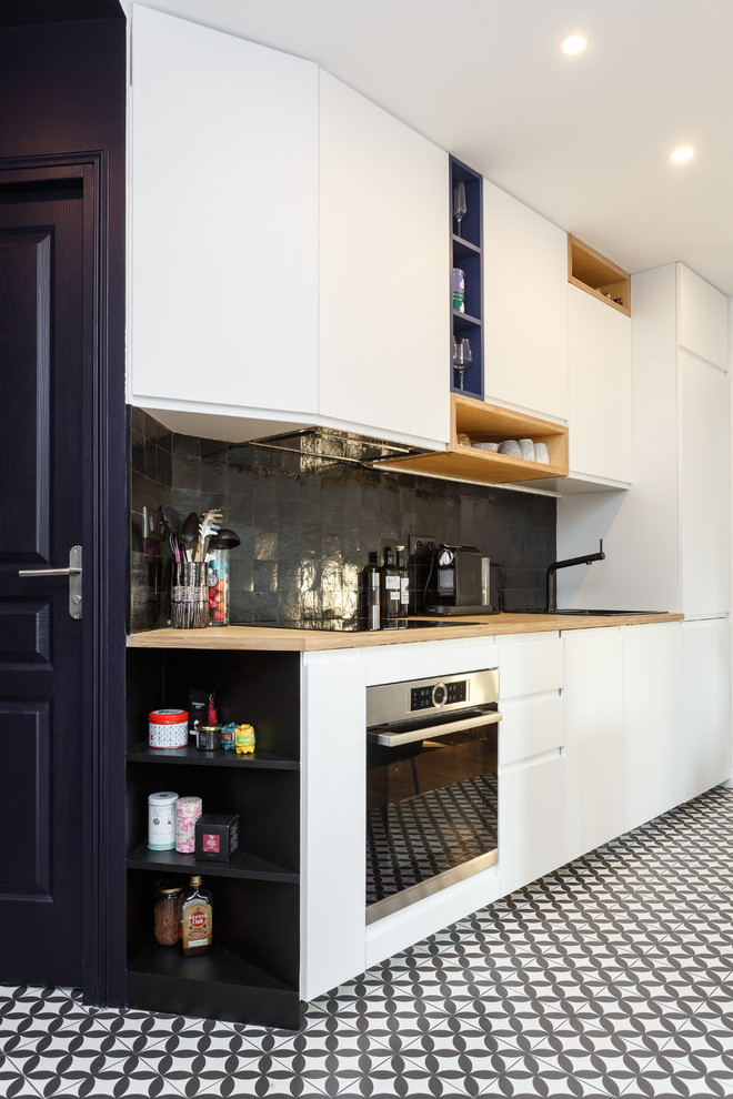 パリにあるお手頃価格の小さなコンテンポラリースタイルのおしゃれなキッチン (シングルシンク、フラットパネル扉のキャビネット、白いキャビネット、木材カウンター、黒いキッチンパネル、テラコッタタイルのキッチンパネル、シルバーの調理設備、セメントタイルの床、アイランドなし、黒い床、ベージュのキッチンカウンター) の写真