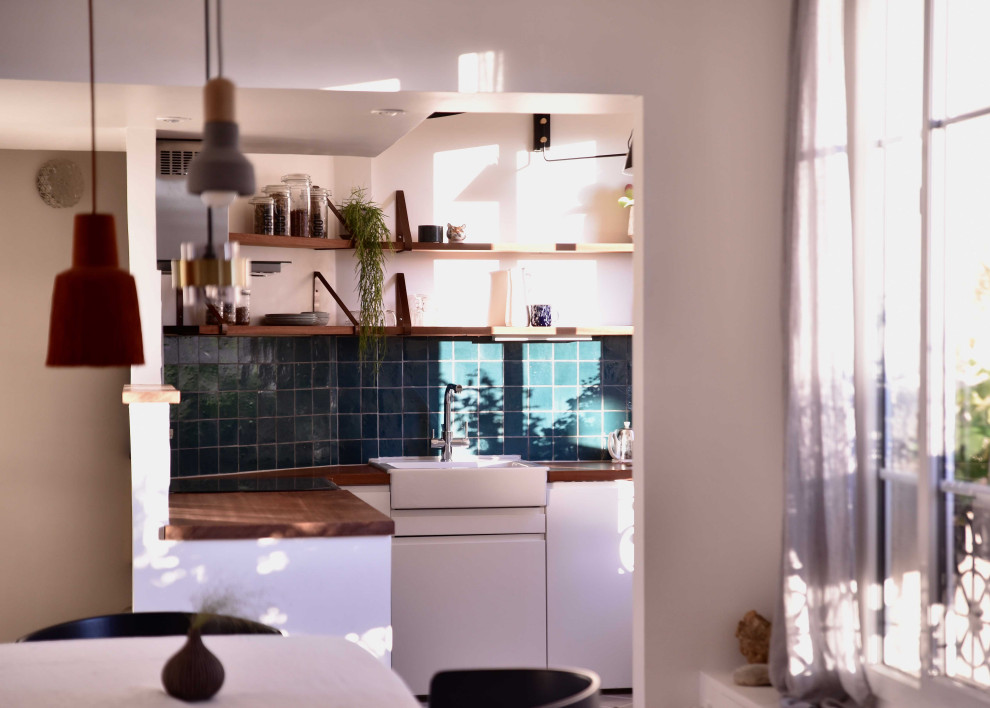Foto på ett litet funkis brun kök, med vita skåp, träbänkskiva, cementgolv, vitt golv, släta luckor, grönt stänkskydd, stänkskydd i terrakottakakel, integrerade vitvaror och en nedsänkt diskho