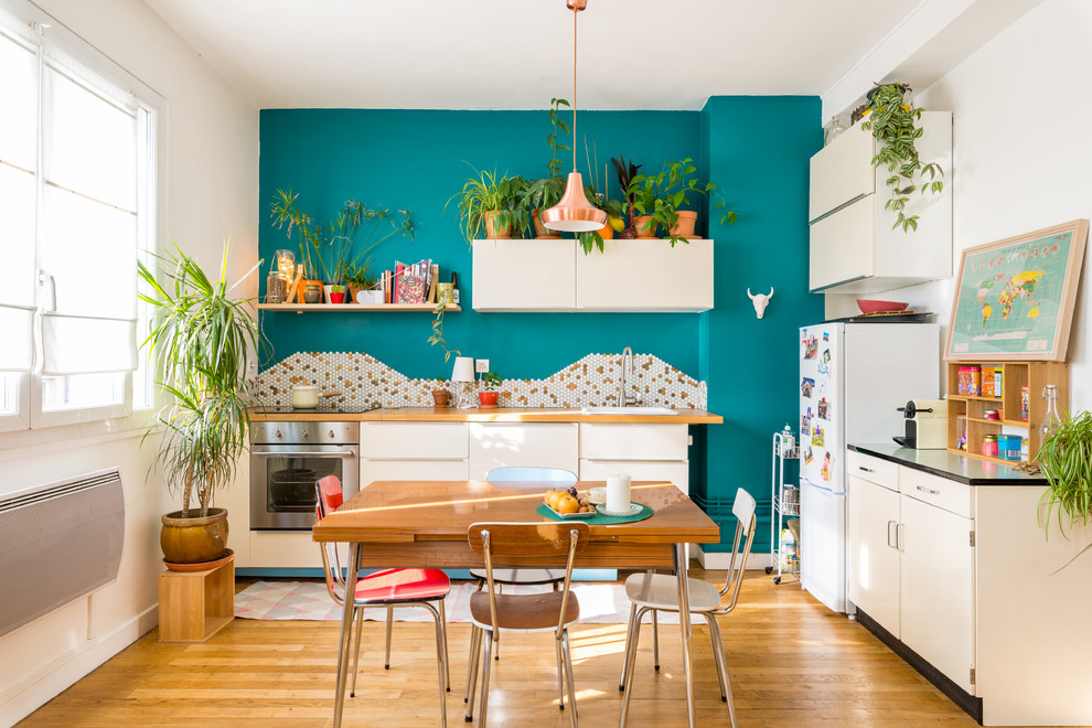 Idées déco pour une cuisine américaine rétro en L avec un évier posé, un placard à porte plane, des portes de placard blanches, un plan de travail en bois, une crédence multicolore, une crédence en mosaïque, un électroménager en acier inoxydable, un sol en bois brun et aucun îlot.