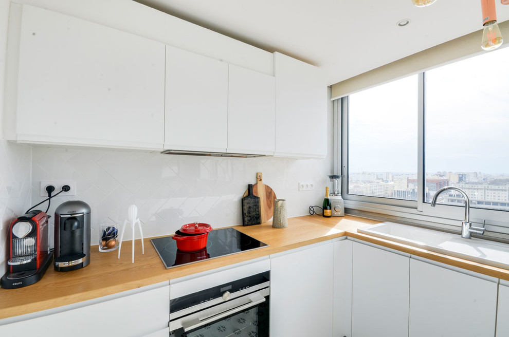 Eat-in kitchen - mid-sized scandinavian l-shaped eat-in kitchen idea in Paris with a single-bowl sink, flat-panel cabinets, white cabinets, wood countertops, white backsplash, ceramic backsplash, stainless steel appliances and no island