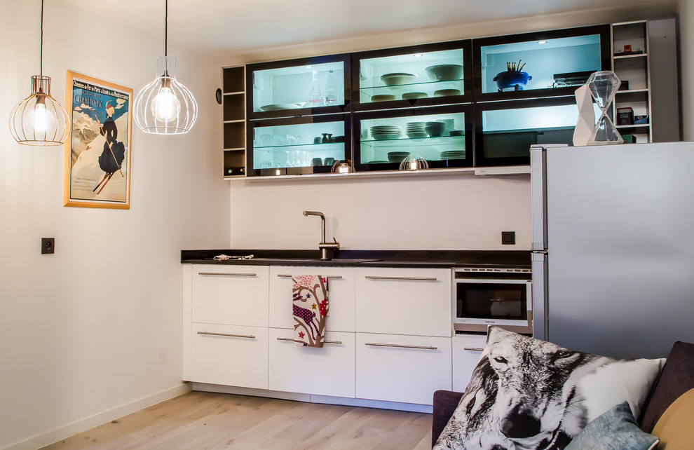 Offene, Einzeilige, Kleine Moderne Küche ohne Insel mit Einbauwaschbecken, weißen Schränken, Küchenrückwand in Schwarz, Elektrogeräten mit Frontblende und hellem Holzboden in Lyon