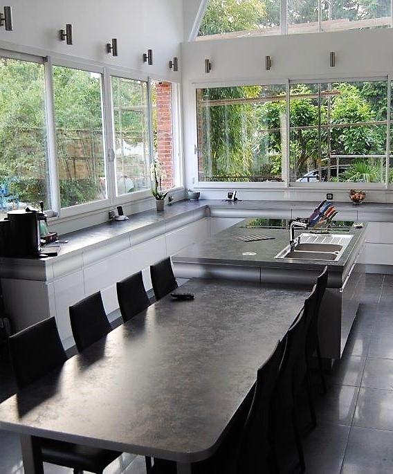 This is an example of an expansive contemporary u-shaped open plan kitchen in Paris with an island, a submerged sink, white cabinets, laminate countertops, stainless steel appliances and ceramic flooring.