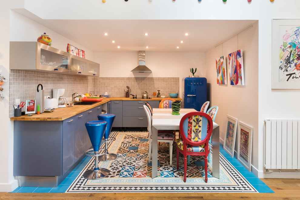 Mittelgroße Stilmix Wohnküche ohne Insel in L-Form mit Einbauwaschbecken, flächenbündigen Schrankfronten, blauen Schränken, Arbeitsplatte aus Holz, Küchenrückwand in Grau und bunten Elektrogeräten in Paris