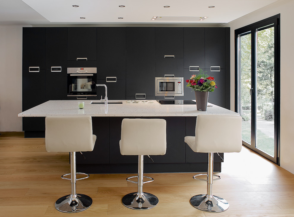 This is an example of a medium sized contemporary galley kitchen/diner in Paris with a submerged sink, flat-panel cabinets, stainless steel appliances, light hardwood flooring, an island, quartz worktops and beige floors.
