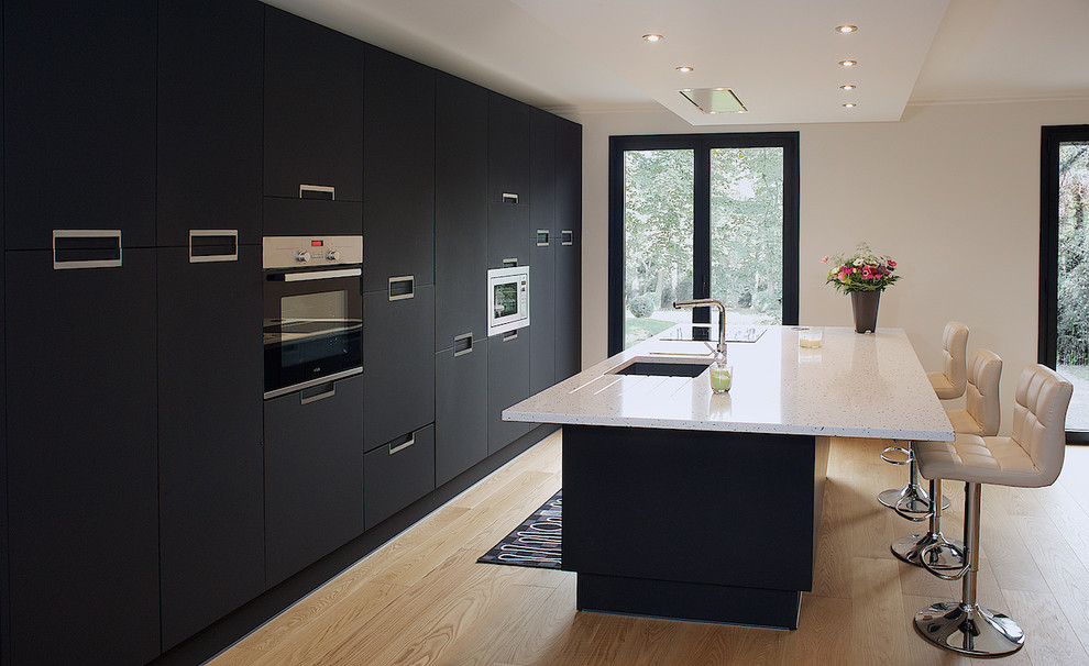 Medium sized contemporary single-wall open plan kitchen in Paris with an integrated sink, flat-panel cabinets, black cabinets, quartz worktops, black splashback, stainless steel appliances, light hardwood flooring, an island and beige floors.