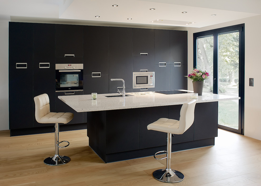 This is an example of a medium sized contemporary single-wall open plan kitchen in Paris with an integrated sink, flat-panel cabinets, black cabinets, quartz worktops, black splashback, stainless steel appliances, light hardwood flooring, an island and beige floors.