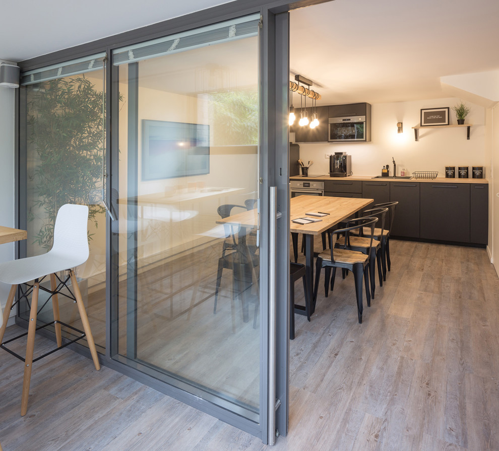 Réalisation d'une cuisine urbaine en L fermée et de taille moyenne avec un évier 1 bac, un placard à porte affleurante, des portes de placard noires, un plan de travail en bois, une crédence blanche, un électroménager en acier inoxydable, un sol en linoléum, aucun îlot, un sol gris et un plan de travail marron.