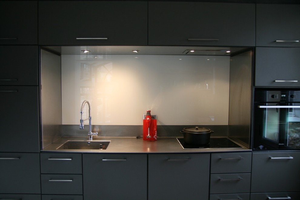Design ideas for a small contemporary single-wall open plan kitchen in Paris with stainless steel worktops, white splashback, glass sheet splashback and black appliances.