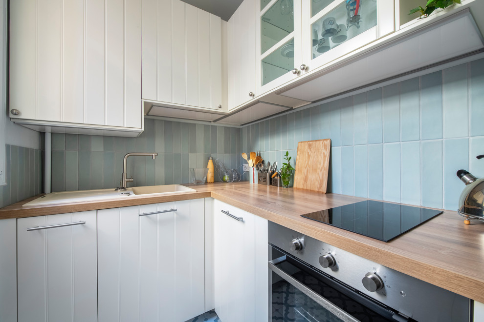 Foto på ett avskilt, mellanstort medelhavsstil beige l-kök, med en enkel diskho, släta luckor, vita skåp, träbänkskiva, blått stänkskydd, stänkskydd i keramik, rostfria vitvaror, cementgolv och blått golv
