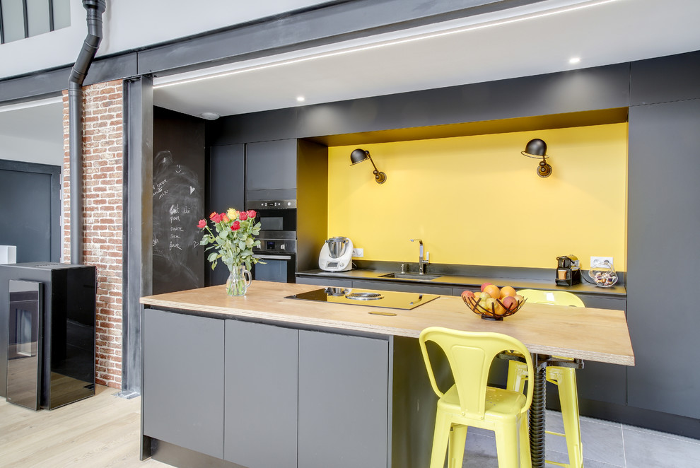 На фото: параллельная кухня-гостиная в стиле лофт с врезной мойкой, плоскими фасадами, серыми фасадами, островом, серым полом и серой столешницей