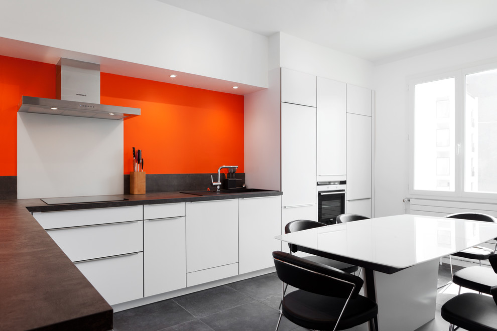 Стильный дизайн: большая угловая кухня в современном стиле с обеденным столом, белыми фасадами, полом из керамической плитки и оранжевым фартуком без острова - последний тренд