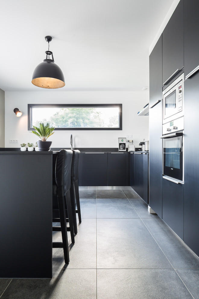 Imagen de cocina actual de tamaño medio con armarios con paneles lisos, electrodomésticos de acero inoxidable, suelo de pizarra, una isla y con blanco y negro