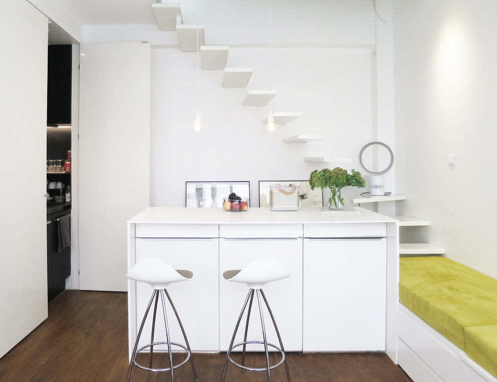 Cette image montre une petite cuisine ouverte linéaire design avec parquet foncé, îlot et des portes de placard blanches.