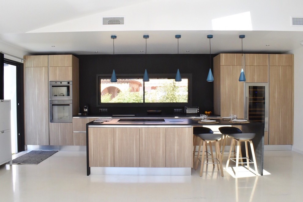 Foto på ett stort funkis kök, med släta luckor, skåp i ljust trä, svart stänkskydd, rostfria vitvaror och en köksö