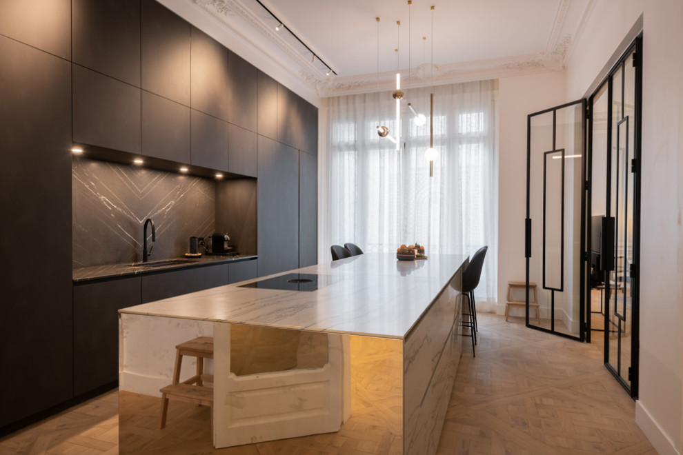 Large contemporary galley enclosed kitchen in Paris with a submerged sink, black cabinets, black splashback, marble splashback, integrated appliances, light hardwood flooring, an island, beige floors, flat-panel cabinets and black worktops.